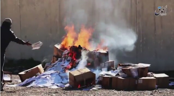 An Islamic State militant tosses Christian textbooks into a bonfire on the grounds that they are the "books of infidels" on March, 10 2016
